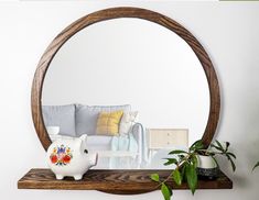 a mirror sitting on top of a wooden shelf next to a potted plant in front of a couch