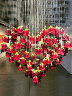 a heart shaped sculpture made out of red flowers in an art gallery with string hanging from the ceiling