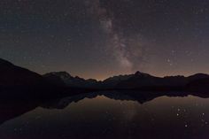 the night sky is filled with stars above mountains and water, as seen from a lake