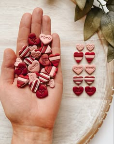 a hand is holding several heart shaped candys on a plate next to some flowers