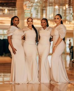 four women in long dresses posing for the camera with one woman wearing a white dress