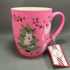 a pink coffee mug with a christmas tree on it and a tag attached to the cup