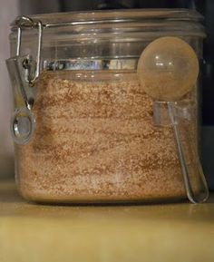 a glass jar filled with brown stuff on top of a wooden counter next to a measuring spoon