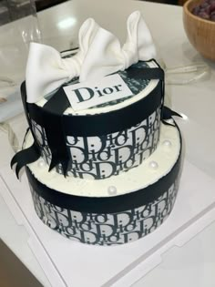 two tiered cake decorated with black and white ribbons on top of a table next to a bowl of grapes