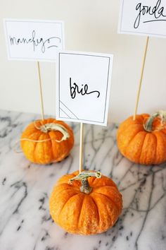 three small pumpkins sitting on top of a table with signs in the shape of them