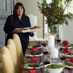 a woman holding a plate with food on it in front of a dining room table