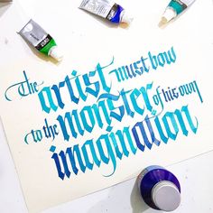 some blue and white lettering on top of a piece of paper next to paintbrushes