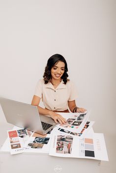 a woman sitting at a table with a laptop computer on top of it, surrounded by magazines