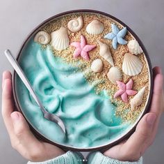 a person holding a bowl filled with blue frosting and seashells on top