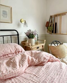 a bed with pink and white sheets in a bedroom next to a mirror, table and chair