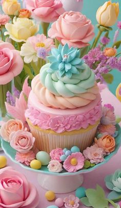 there is a cupcake decorated with pink and blue frosting on the top, surrounded by flowers