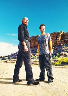 two men are standing in the middle of a dirt road and one is wearing sunglasses