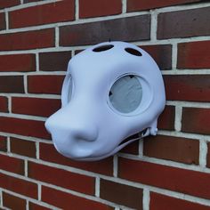 a white mask mounted to the side of a brick wall