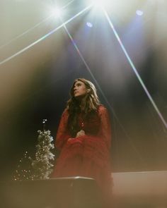 a woman in a red dress is sitting on a table with a lit christmas tree behind her