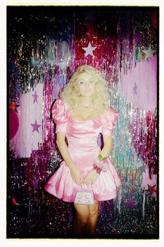 a woman in a pink dress standing next to a wall with stars and confetti on it