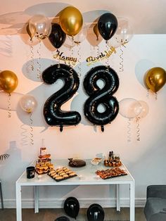 a table topped with black and gold balloons next to a number 28 sign on the wall