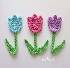 three crocheted tulips sitting side by side on a white surface, one is pink, the other is blue