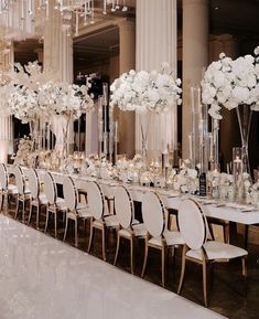 a long table with white flowers and tall vases filled with candles sits in the middle of an elegant ballroom