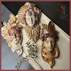 three decorative wall hangings with faces and leaves on them in gold, white and pink colors