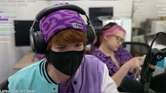 two people sitting in front of a microphone wearing headphones and covering their faces with a black mask