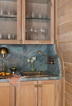 a kitchen with wooden cabinets and marble counter tops, along with glass shelves filled with wine glasses