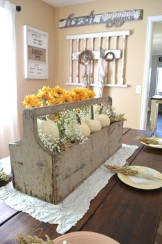 a wooden crate filled with pumpkins and flowers on top of a table next to plates