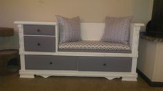 a white bench with grey drawers and two gray pillows on it's seat area