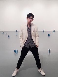 a man standing in front of a white wall with blue letters on it and wearing glasses