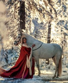 a woman in a red dress standing next to a white horse on a snowy field