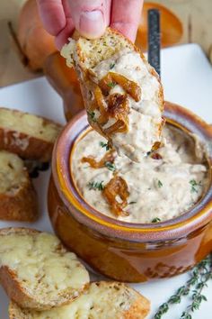 a person dipping something into a bowl of dip with bread on the side and carrots in the background