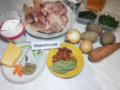 a table topped with plates and bowls filled with food next to bottles of liquid, butter, eggs, carrots, potatoes and other ingredients