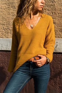 a woman standing in front of a wall wearing jeans and a sweater