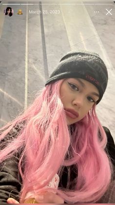 a woman with pink hair wearing a black beanie and looking at her cell phone