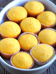 a white bowl filled with yellow cupcakes on top of a wooden table