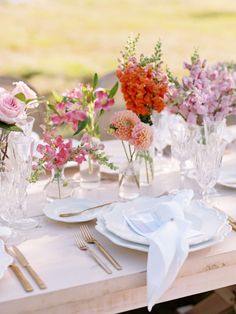 the table is set with white plates, silverware and pink flowers in vases