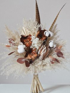 an arrangement of dried flowers and feathers in a vase