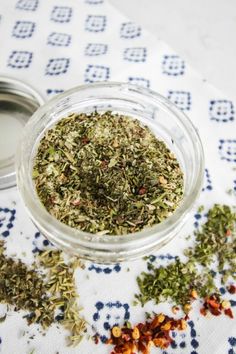 a glass bowl filled with herbs on top of a table cloth next to a metal container