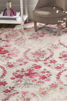 a white and pink rug with flowers on the floor in front of a gray chair