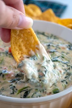 a hand dipping a tortilla chip into a bowl of spinach and cheese dip