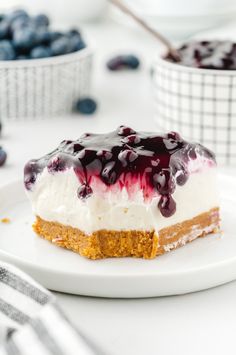 a piece of cheesecake on a plate with blueberries in the bowl behind it