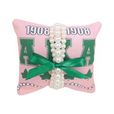 White or pink pearl bracelets on pink and green themed 4in x 4in AKA jewelry pillow. The perfect gift for any member of AKA. Each gift set comes with a three strand bracelet set and removable bow.  Produced by a Black-owned business and member of the Divine Nine. Pink And Green Jewelry, Aka Paraphernalia, Aka Sorority Gifts, Pink Pearl Bracelet, Aka Sorority, White Pearl Bracelet, Handmade Sandals, Sorority Gifts, Alpha Kappa Alpha