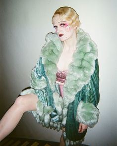 a woman in a green fur coat posing for the camera with her legs spread out