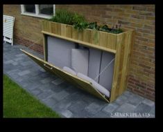 a wooden planter filled with lots of plants next to a brick wall and grass