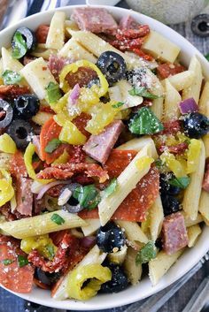 pasta salad with olives, tomatoes, and ham in a white bowl on a wooden table