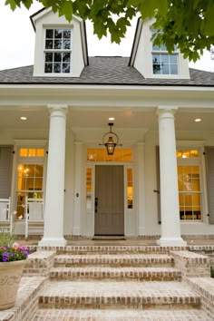 a house with columns and two windows on the front, and stairs leading up to the second floor