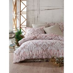 a bed with pink comforter and pillows in a room next to a plant on the floor