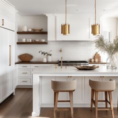 two stools sit at the center of a kitchen island with white cabinets and gold accents