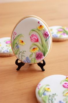 three decorated cookies sitting on top of a wooden table next to each other with flowers painted on them