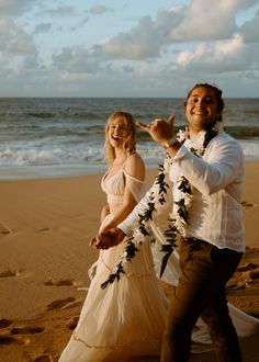 a man and woman standing on top of a sandy beach next to the ocean holding hands