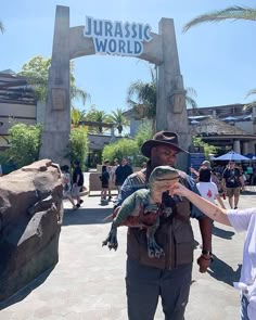 a man holding a small lizard in front of a sign that says jurasic world